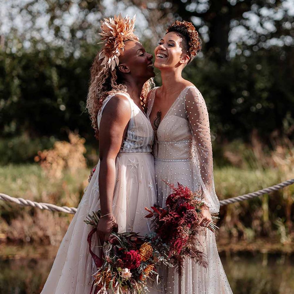Bride in golden leaf crown and sleeveless peach gown with star embroidery laughing with bride in crystal embellished gown and gold headdress 