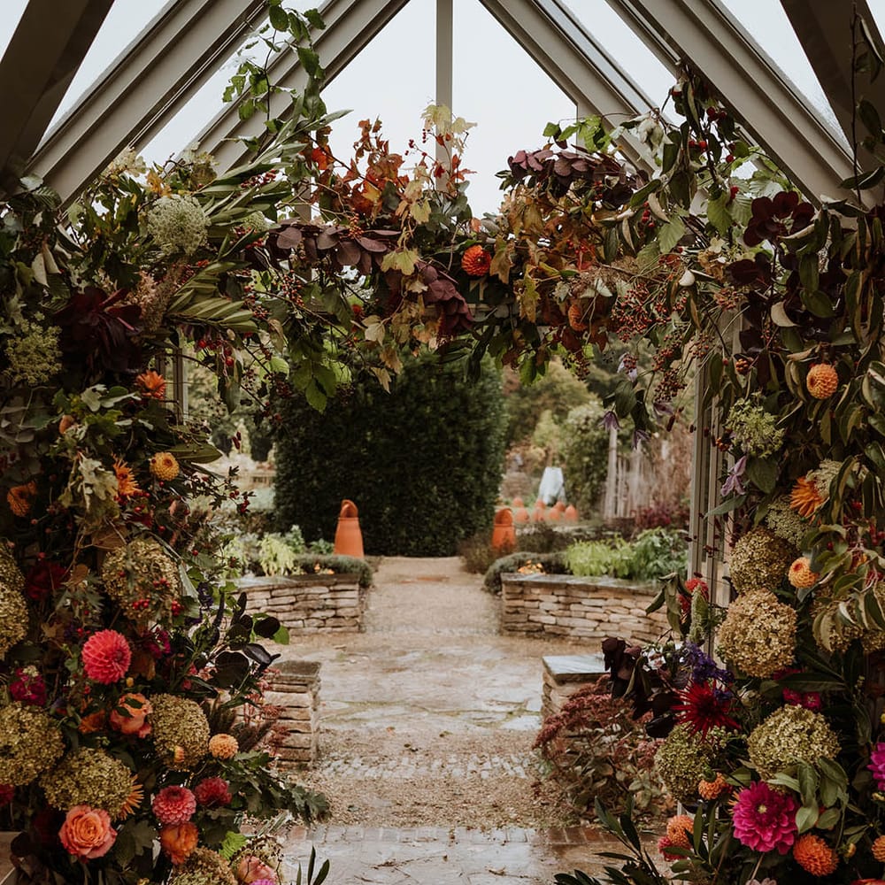 Large luxe floral arch with white and pink carnations, garden roses, red strawflower, eucalyptus, baby’s breath and various dried flowers  