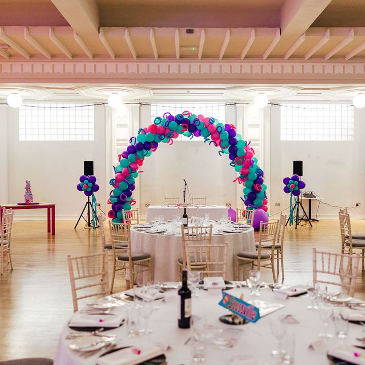 Reception room of theme park wedding at Margate Dreamland with blue, pink and purple balloon arches and columns, large speakers and a neutral tablescape theme 
