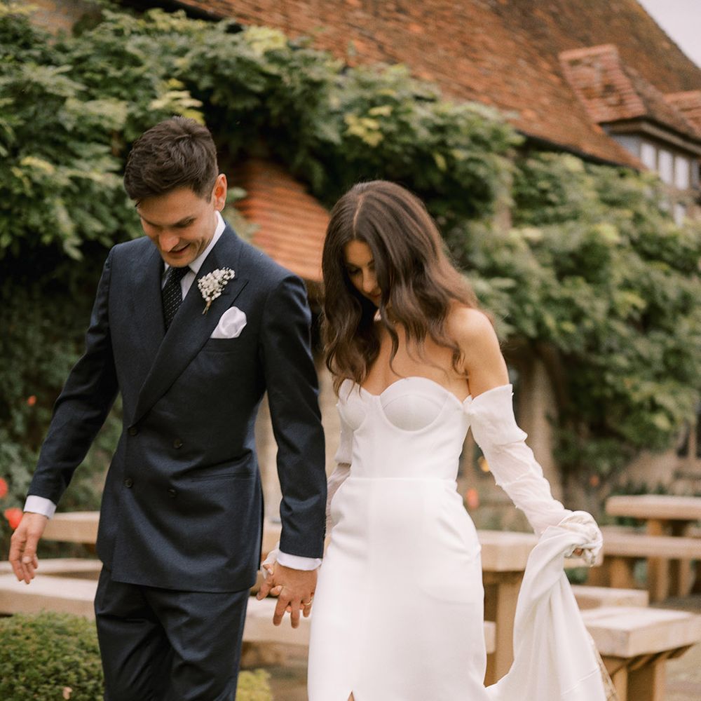 The bride walks in her platform Jimmy Choo pearl shoes in a modern strapless wedding dress with the groom in a navy suit 