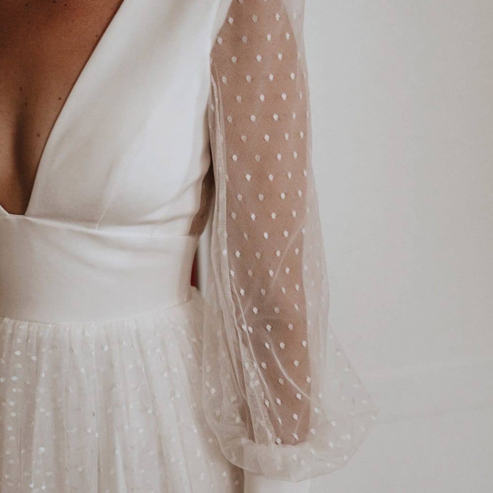 A Sassi Holford wedding dress with long sheer sleeves with polka dots on with a deep neckline 