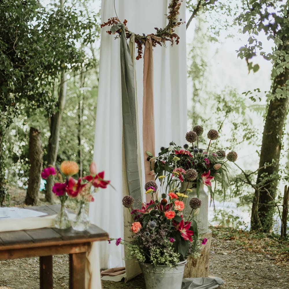 Woodland wedding with floral hoop decor, greenery, and pots of pink flowers with echinops