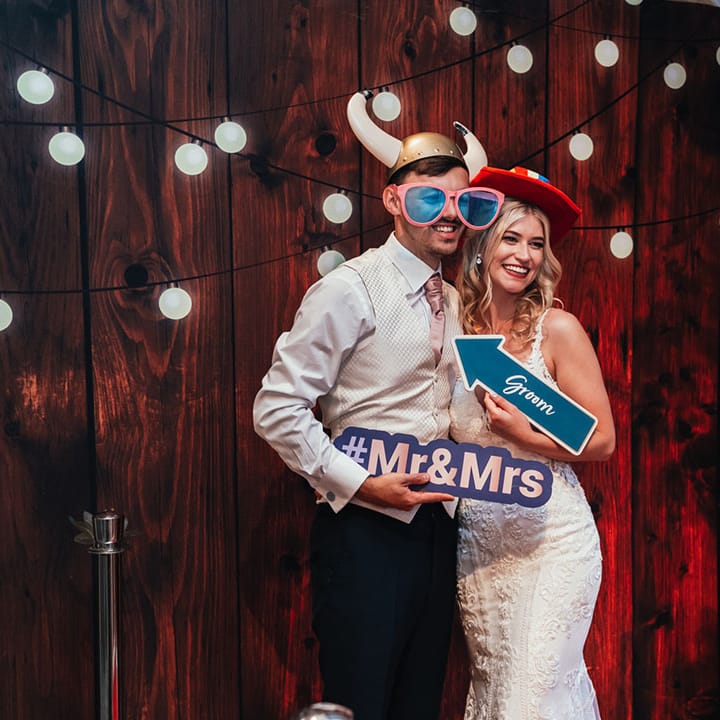 The bride and groom pose together with silly and fun props for their photo booth wedding entertainment 