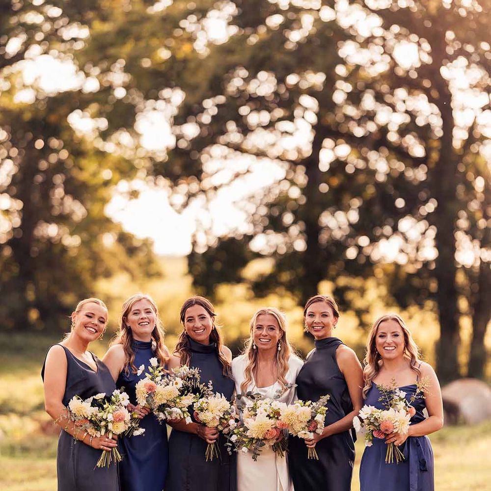Bride in short sleeve satin wedding dress standing with bridal party in mismatched navy bridesmaid dresses 