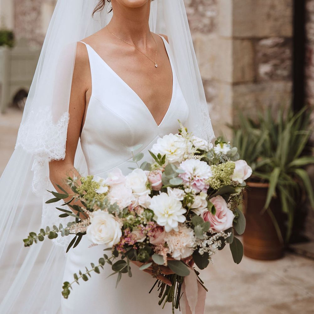 Bride wearing satin plunging wedding dress holding blush pink and white wedding bouquet 