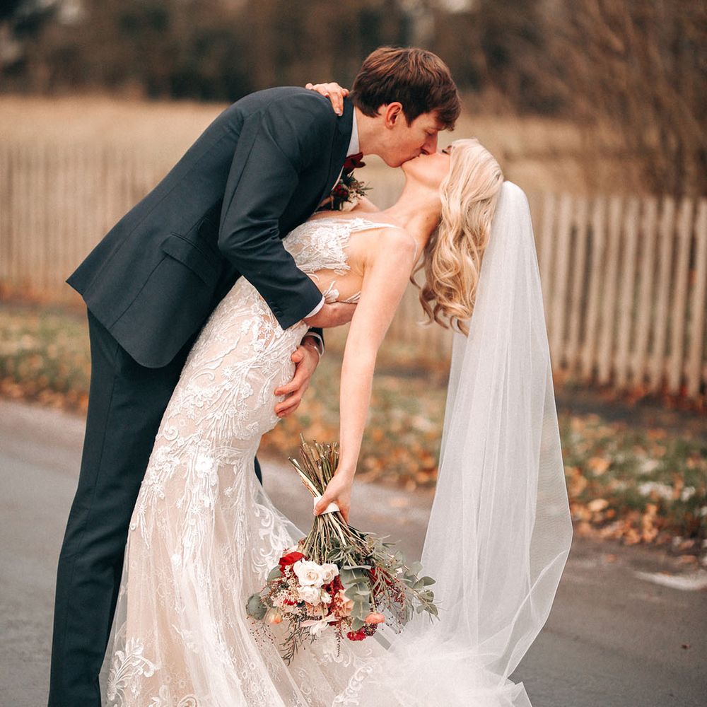 Groom in navy suit kisses bride in lace illusion wedding dress for wedding couple portrait 