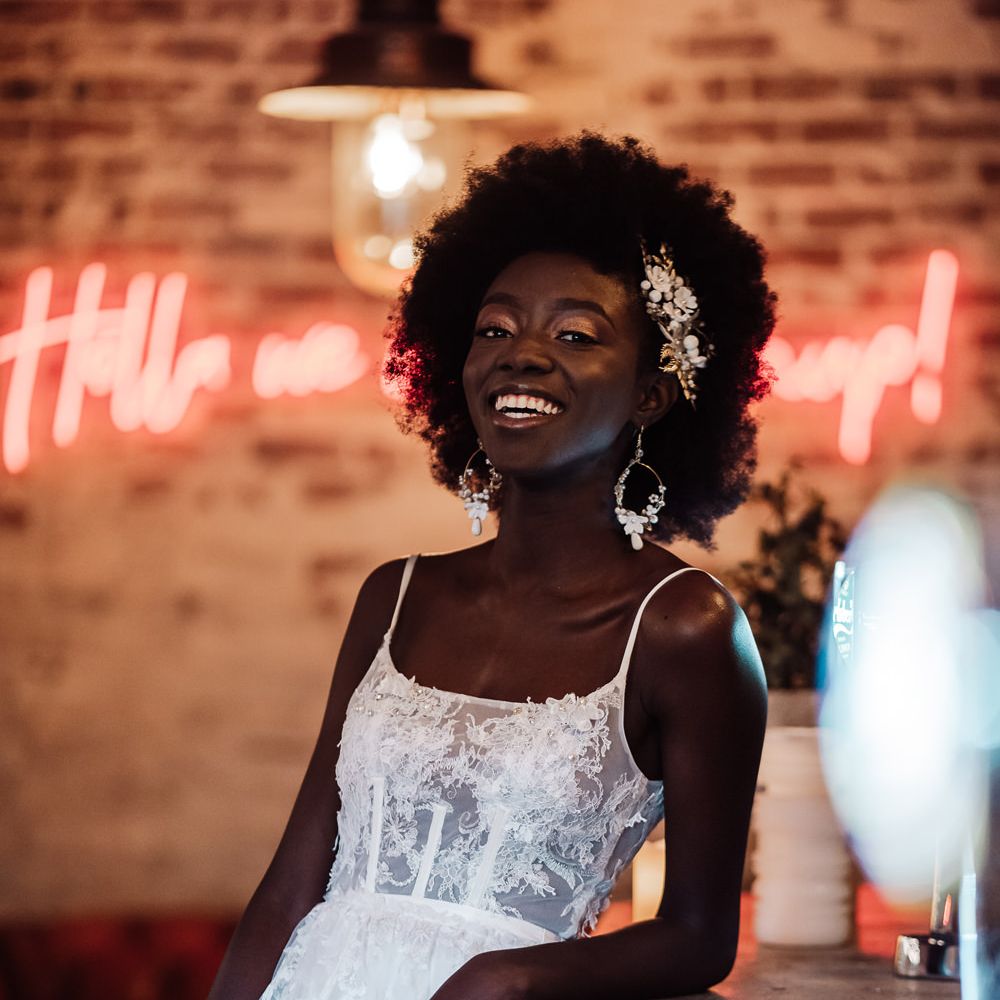 Black bride in a fitted wedding dress with lace bodice smiling at the bar with a neon sign in the background