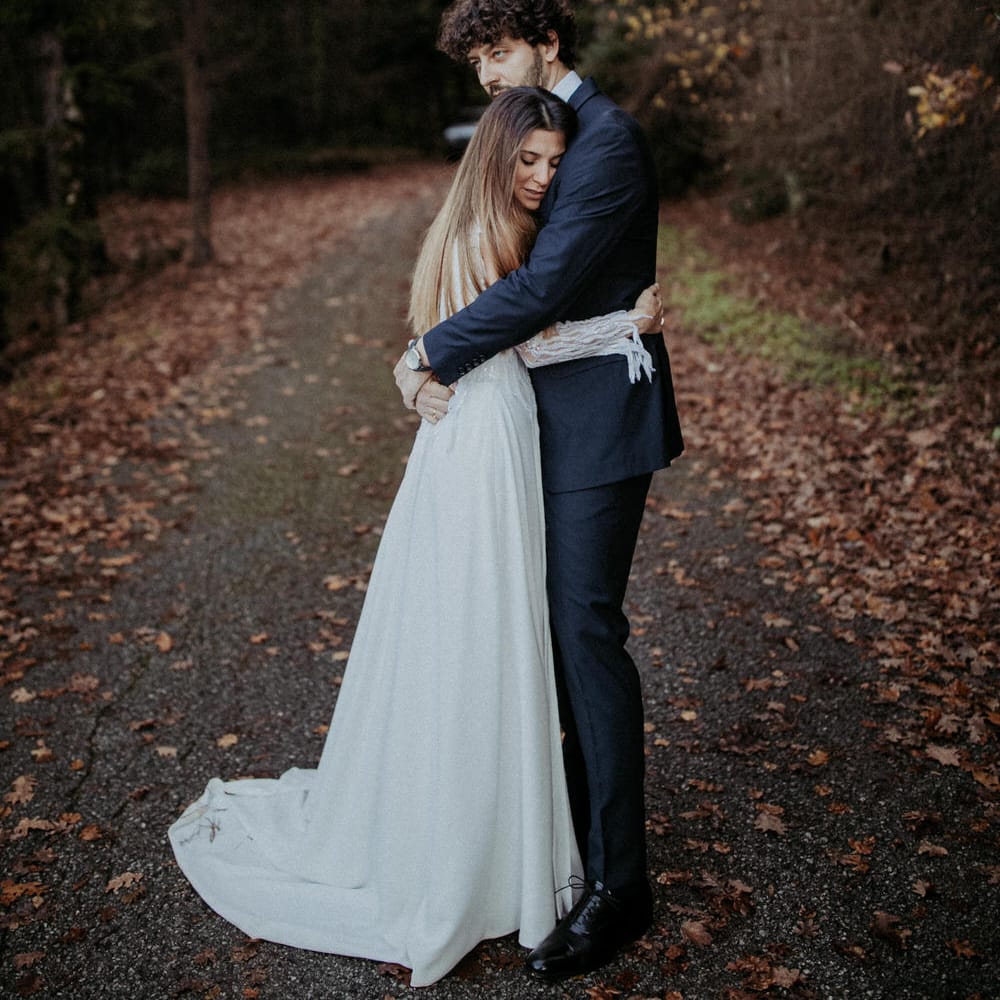 The bride and groom embracing on a leafy road surrounded by trees