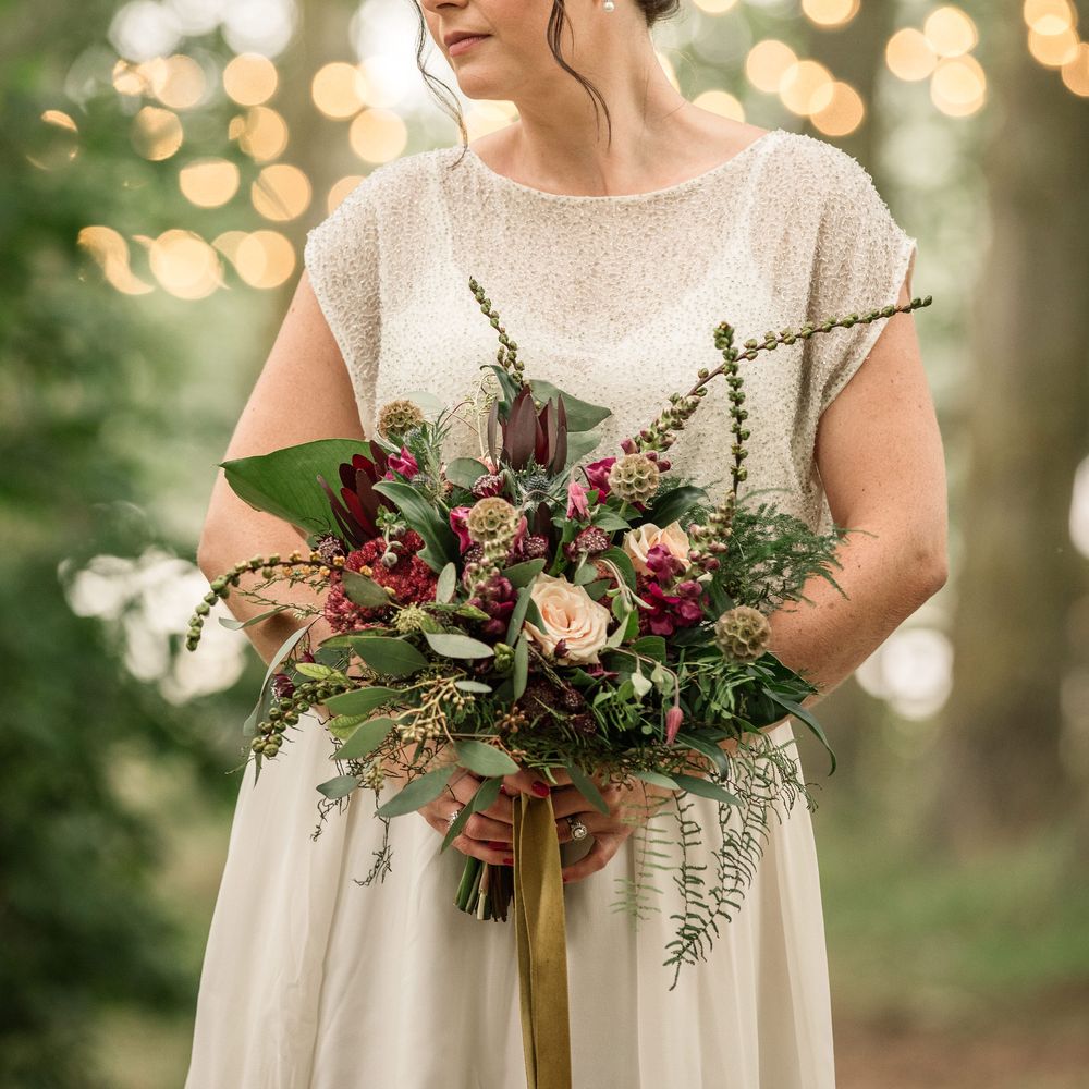 Bride carries floral bouquet and wears her hair in low updo with curls around face