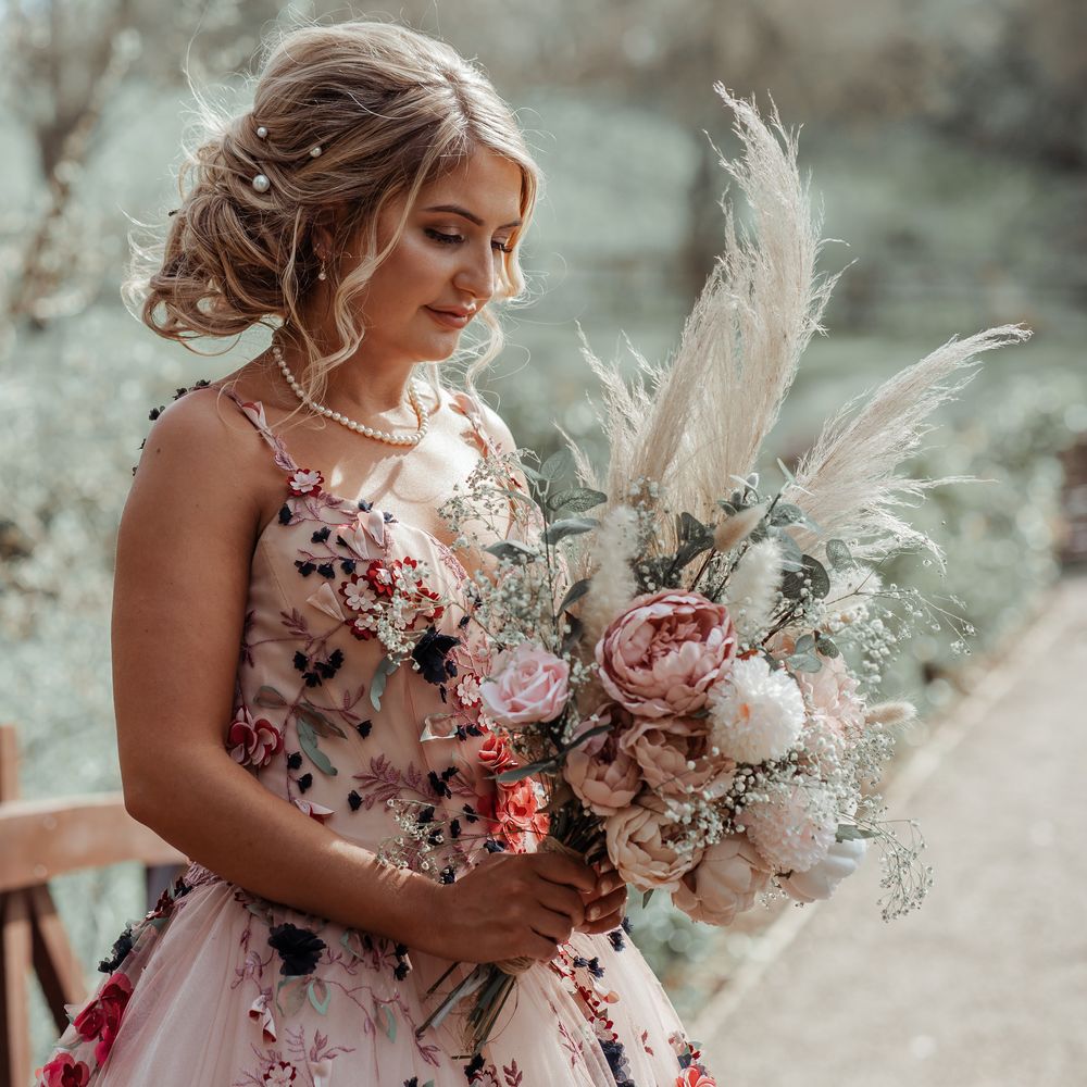 Bride stands with floral bouquet filled with blush pink peonies and pampas grass