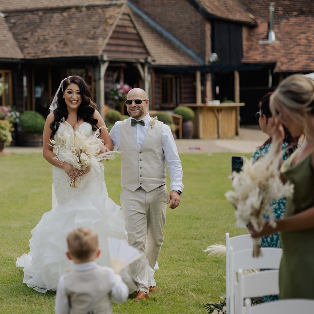 Bride in a Mori Lee mermaid wedding dress walking down the aisle being greeted by her son in a beige suit 