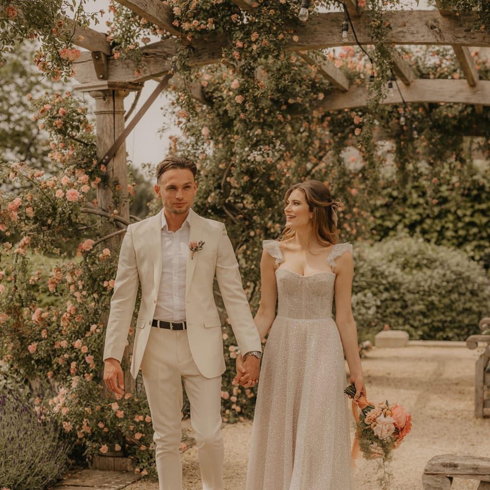 Bride in a sparkly Made With Love dress holding hands with her groom in a stone coloured suit 
