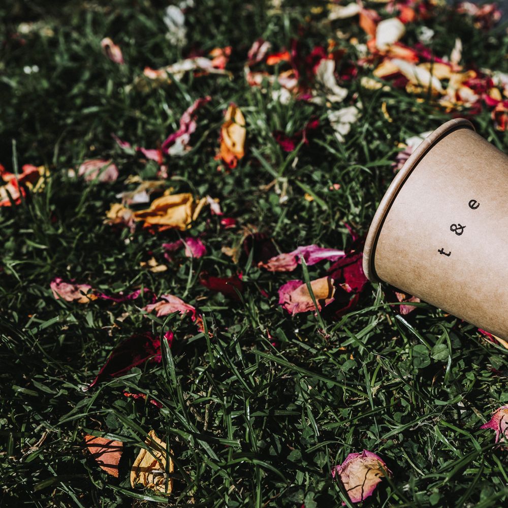 Hand pressed brown cup with initials next to dried confetti on grass