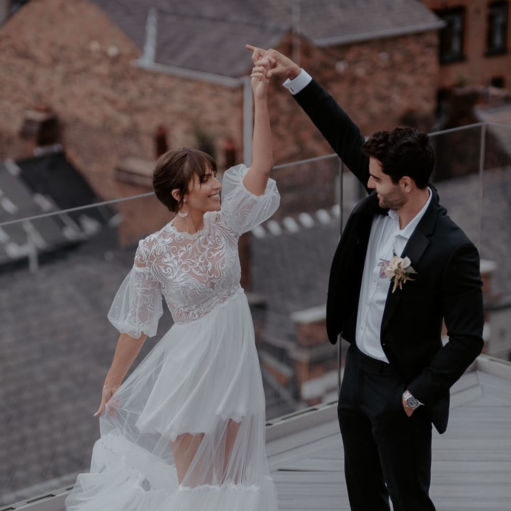 Groom in a black suit and orchid buttonhole twirling his bride in a tulle wedding dress with chic bridal up do 