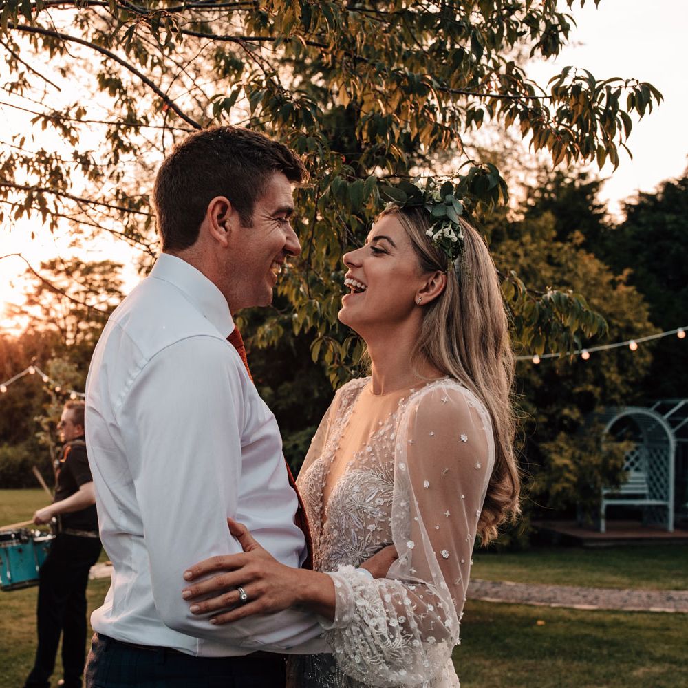 Bride in long sleeve embroidered Julie Vino wedding dress and boho flower crown dances with groom in white shirt during golden hour at wedding reception