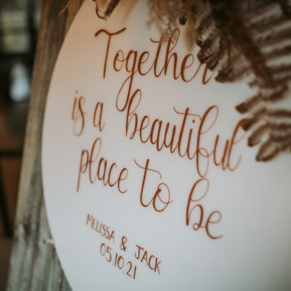 Round wedding sign reading 'Together is a beautiful place to be' on wooden board with ferns for rustic wedding