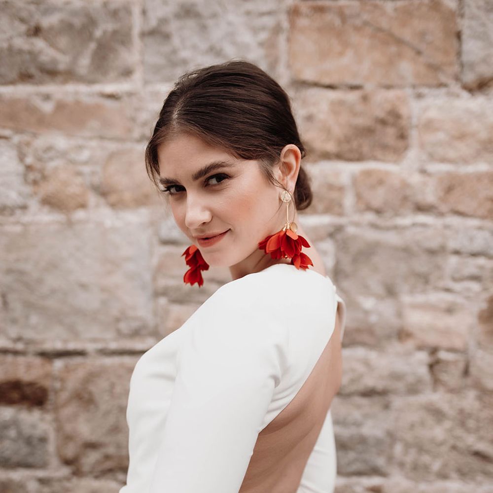 Bride in an open back wedding dress with long sleeves and button detail wearing red statement earrings and tied back hair 
