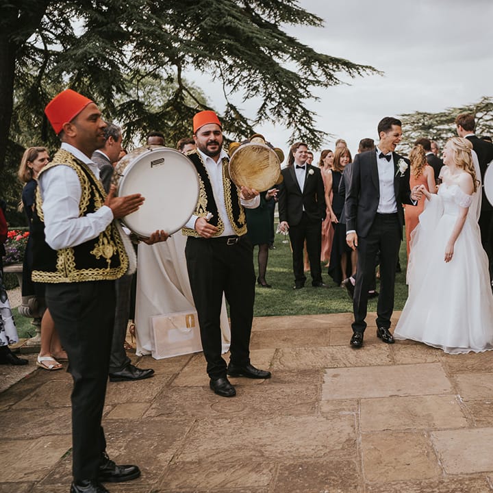 Bride and groom laugh outside their wedding venue with their Zaffa band 