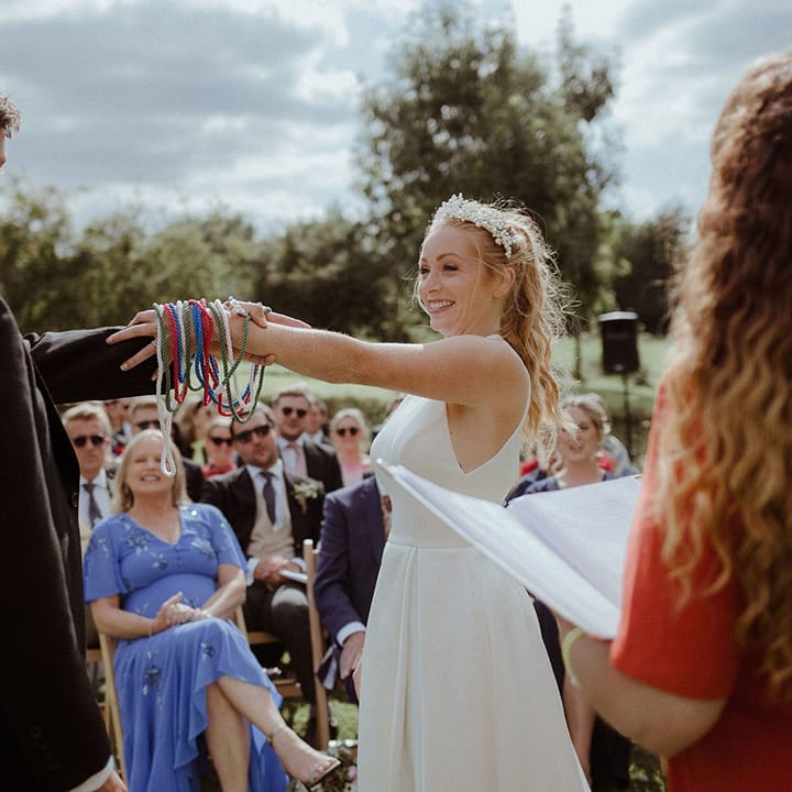 Bride and groom participate in hand fasting ceremony on their wedding day with red, green, blue and white ropes 