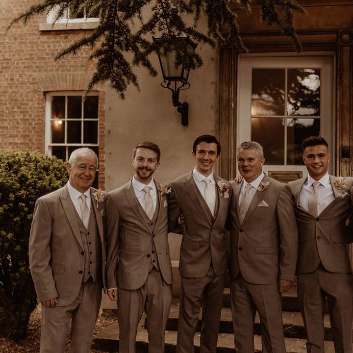Groom and groomsmen stand with their arms around each other in matching wedding suits 