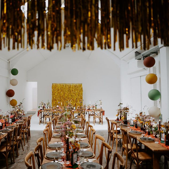 Wooden banquet tables with small floral arrangements and orange fabric table runners