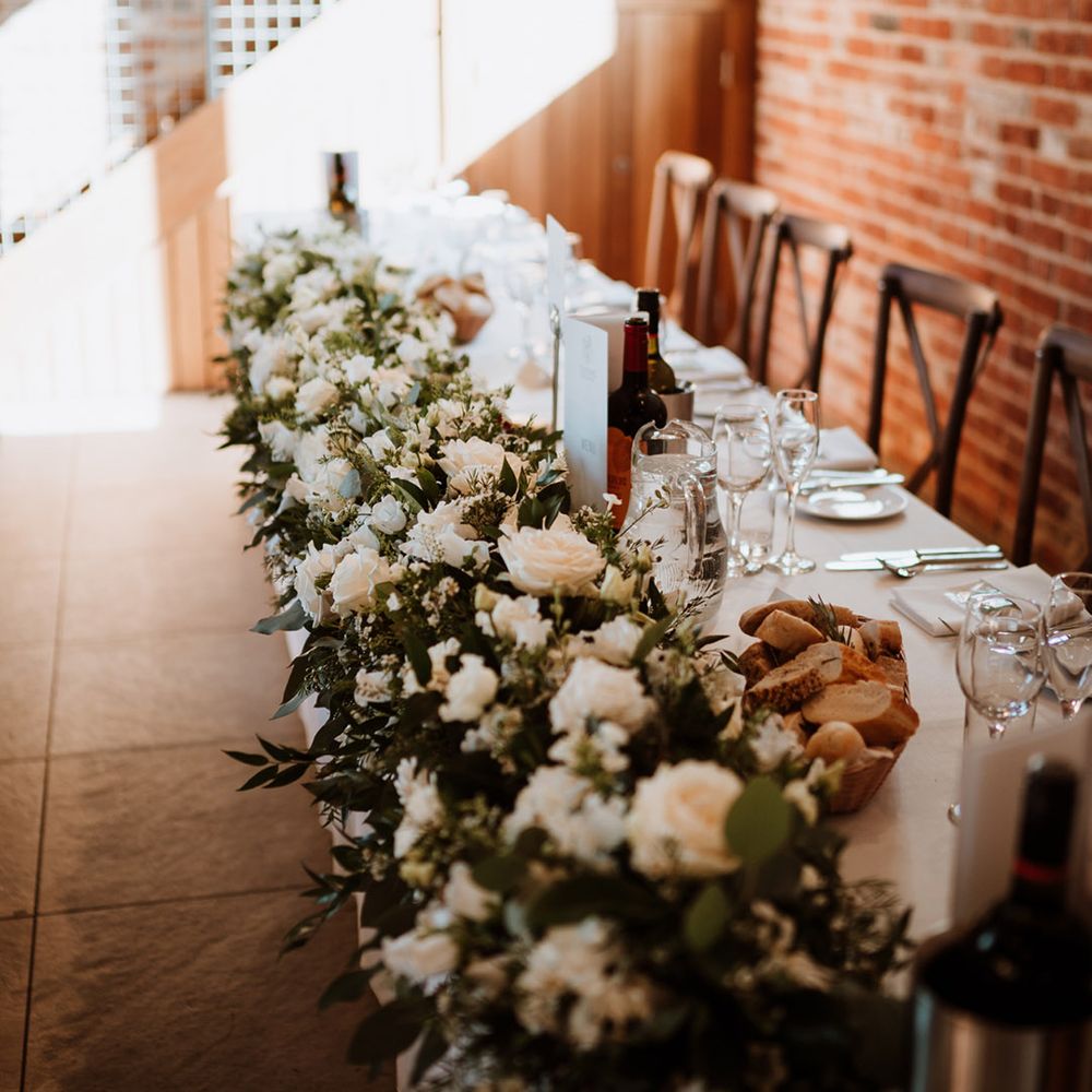 Large white rose and greenery display along the top table for the wedding reception 
