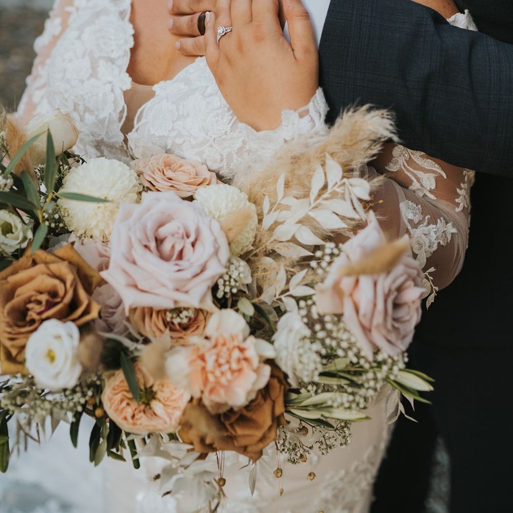 Groom embraces bride in long sleeve lace wedding dress holding pastel bouquet 