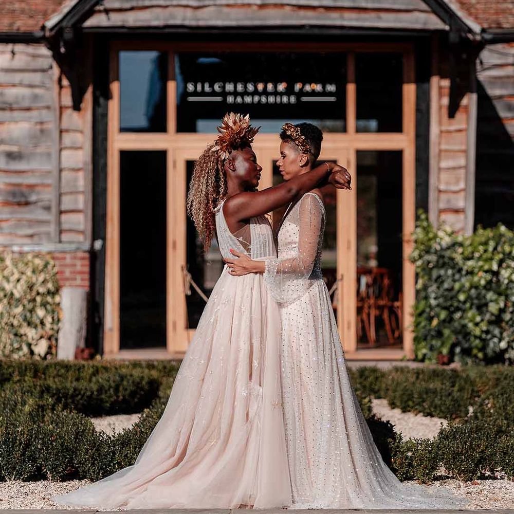Brides in sleeveless floaty peach gown with embroidered stairs and crystal embellished gown and gold headdress embracing outside Silchester Farm