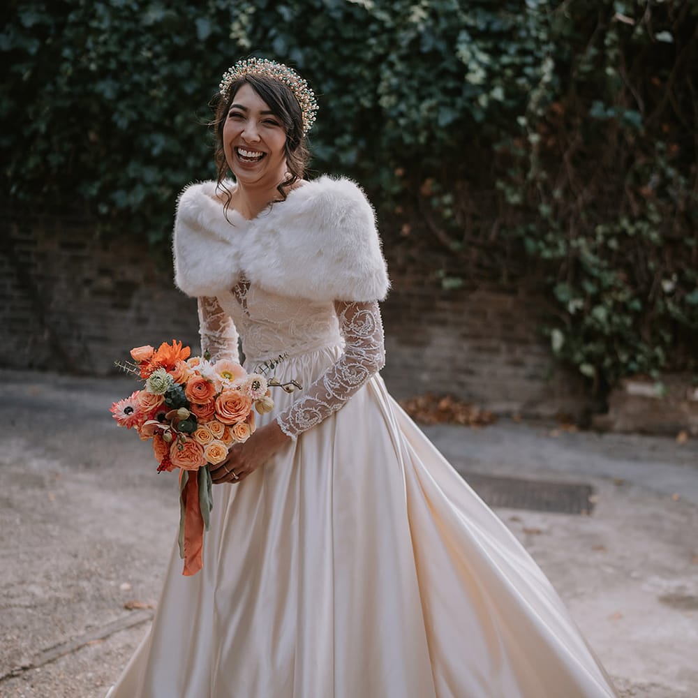 Bride wearing taffeta material princess wedding dress with long lace sleeves  and cropped faux fur bridal cover up and gold, pearl and emerald bridal crown 