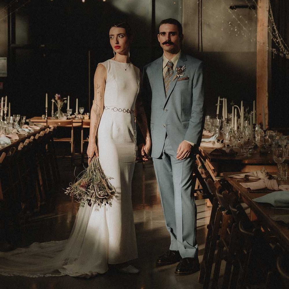Lisa in fitted pre loved wedding dress with open back holding DIY floral bouquet and standing beside Gabriel in powder blue Gucci suit 