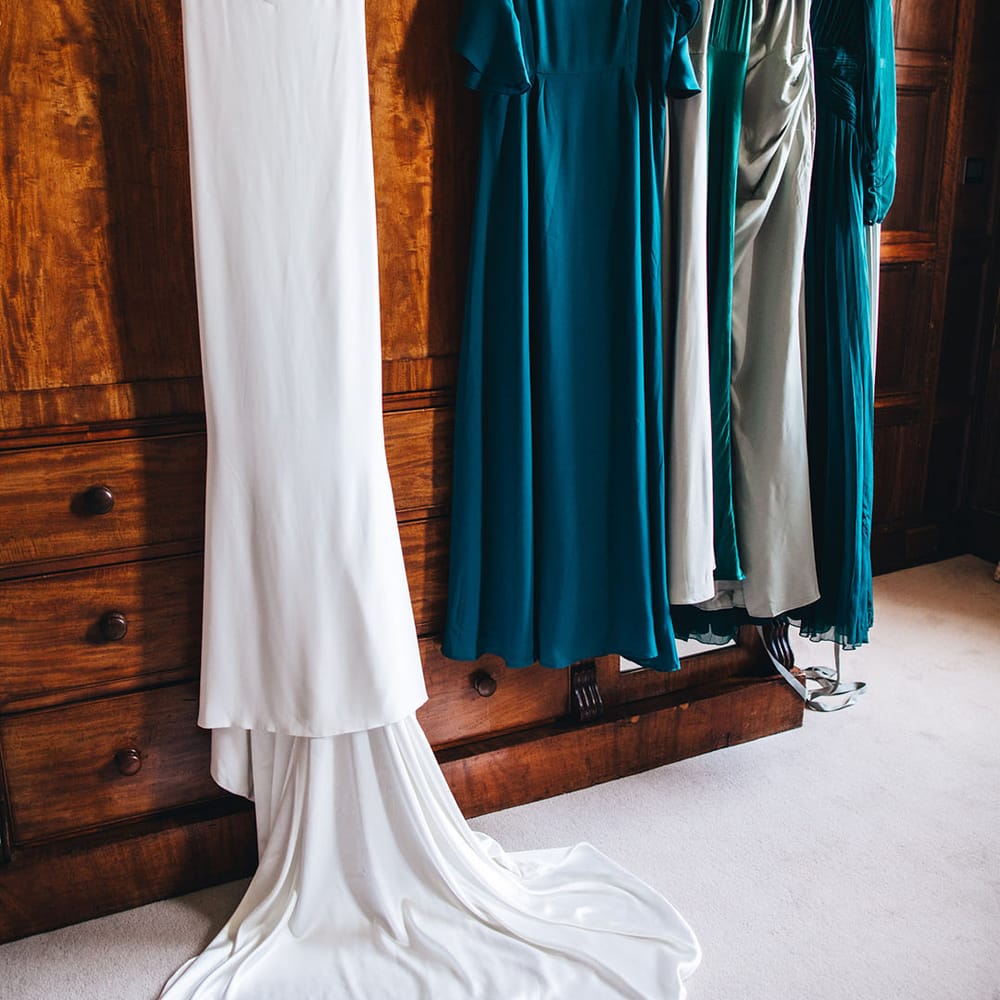 The bride's satin wedding dress hanging up with the bridesmaids dresses in different shades of green 