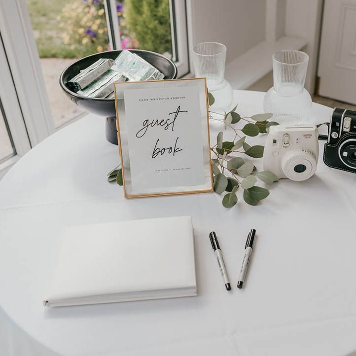 White wedding guest book and white polaroid camera with black and white sign with gold photo frame 