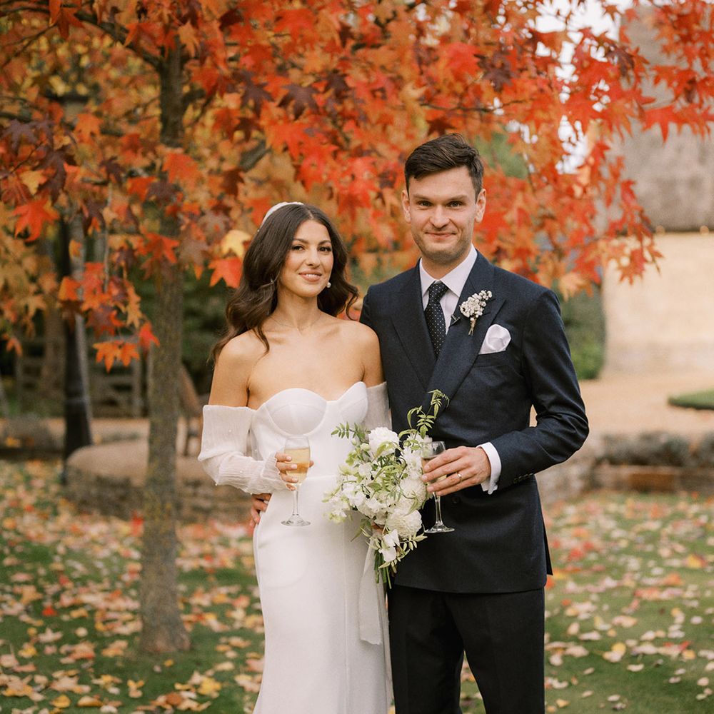 Groom in dark suit and tie dirking a glass of champagne with the bride in a strapless wedding dress with detachable sleeves and white wedding bouquet