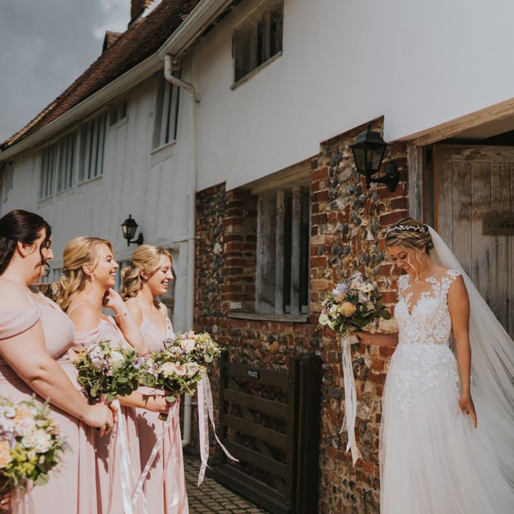 Bride in illusion lace wedding dress with her blonde hair in braided hairstyle with bridesmaids in pink bridesmaid dresses seeing her for the first time 