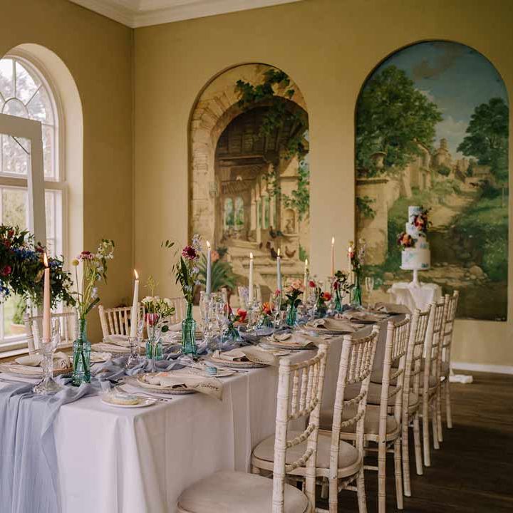 Classic wedding tablescape at Braxted Park wedding venue with white wedding tablecloth, cornflower blue wedding table runner, bright blue glass bottles with dried flowers, pastel tapered candles and spring floral arrangements 