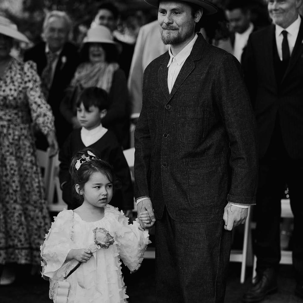 Groom standing with little flower girl in white butterfly dress 
