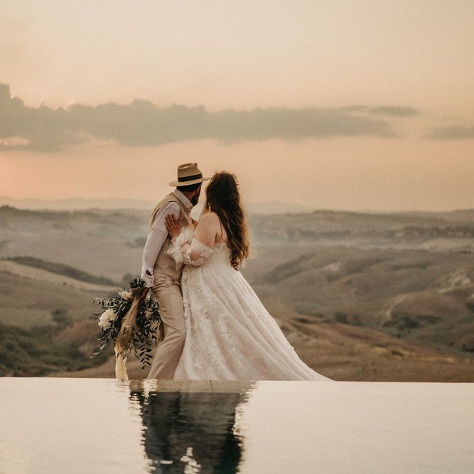 Groom holding olive bouquet as they look over Tuscany countryside