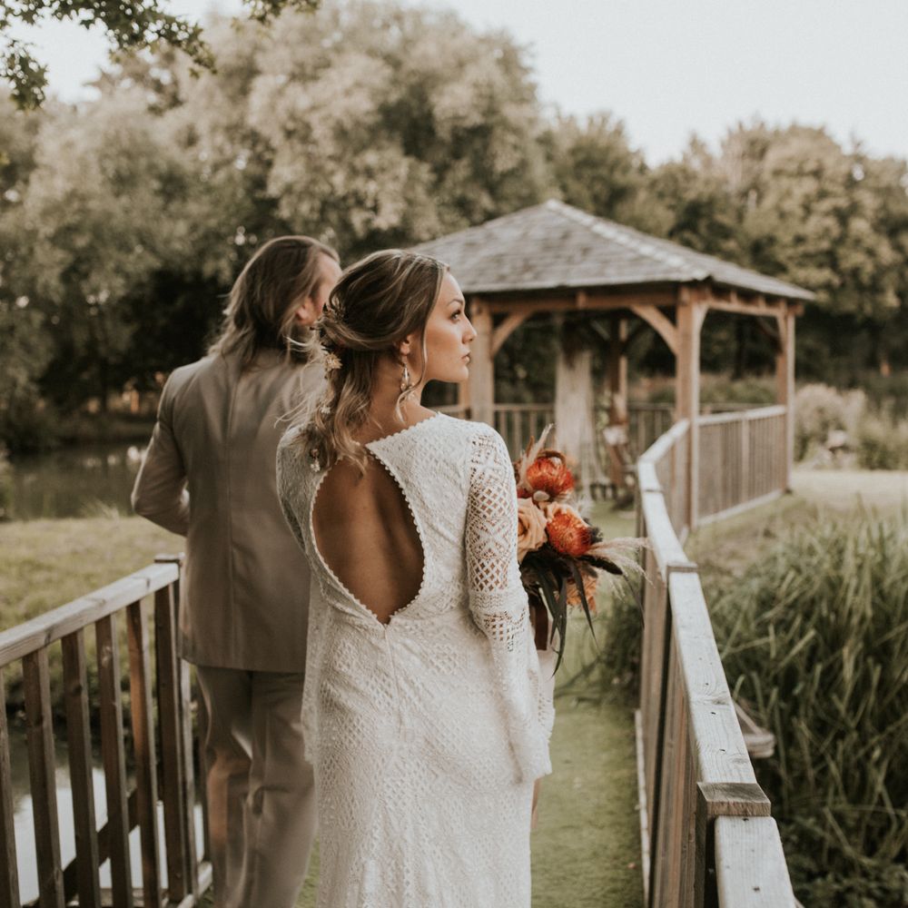 Bride & groom walk together with bride wearing open back dress with scalloped edge