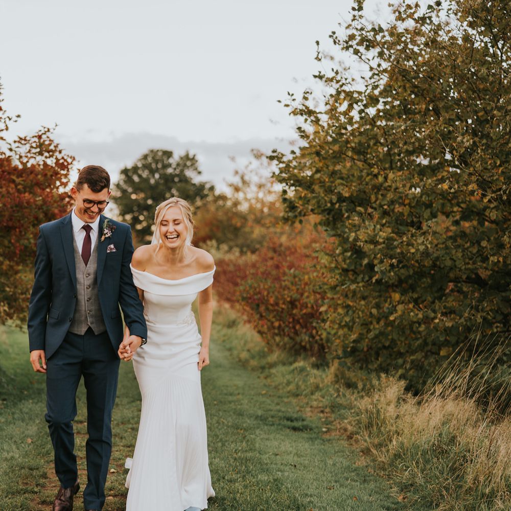 Bride & groom walk together through countryside surrounded by greenery