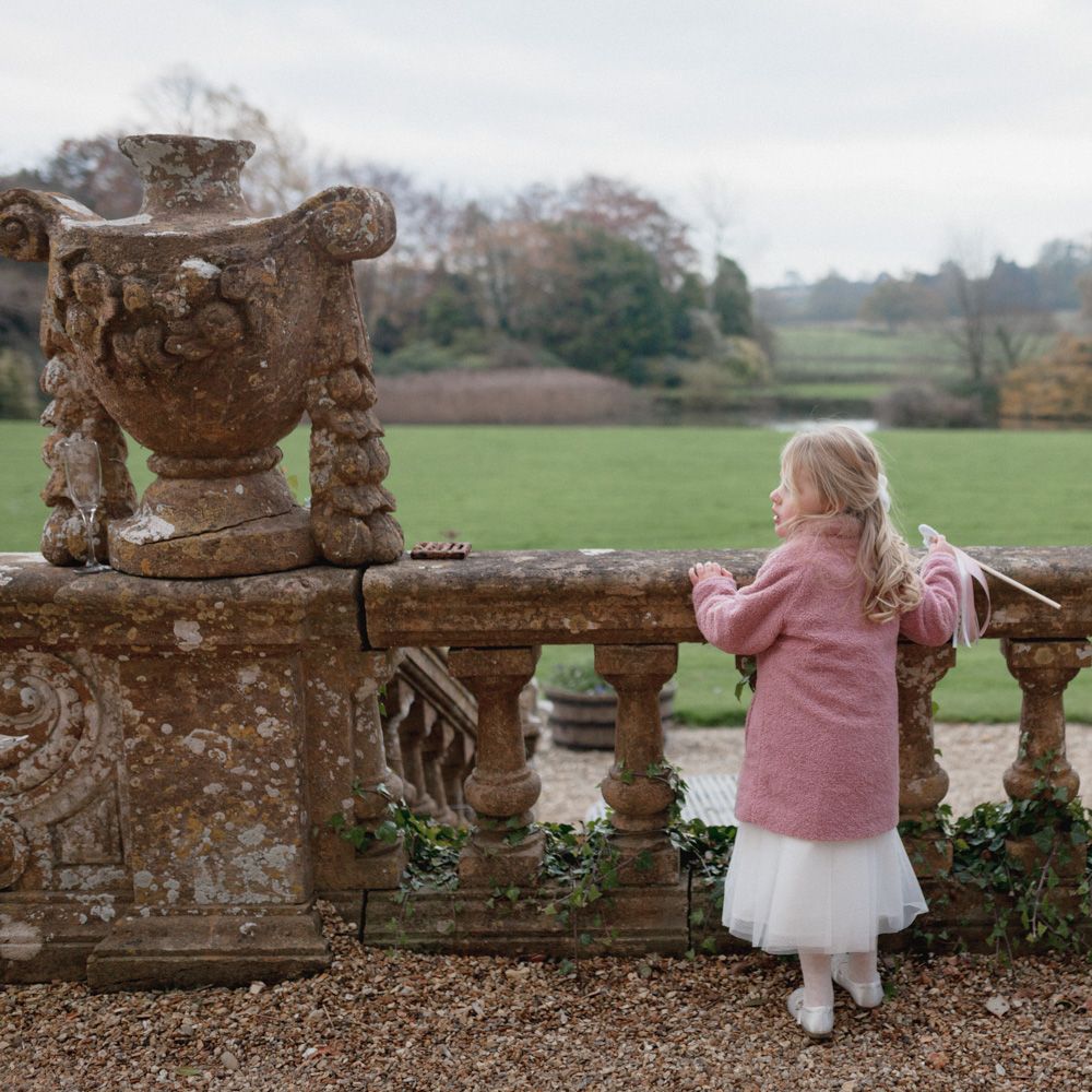 Child at Brympton House wedding wearing pink coat, tulle white skirt and silver ballerina shoes