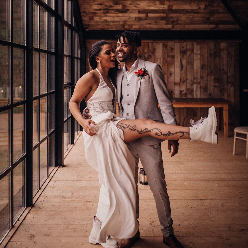 Bride lifts leg wearing white wedding Dr Martens as groom stands beside her 