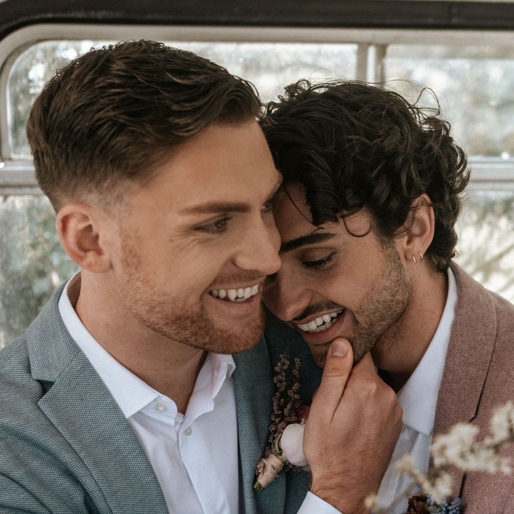 Grooms laugh outdoors during wedding day whilst wearing pastel suits