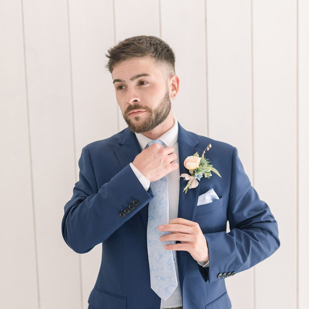 Stylish groom at a summer wedding in beige chinos, white shirt and navy blazer with a peach flower buttonhole and pastel blue tie and pocket square 