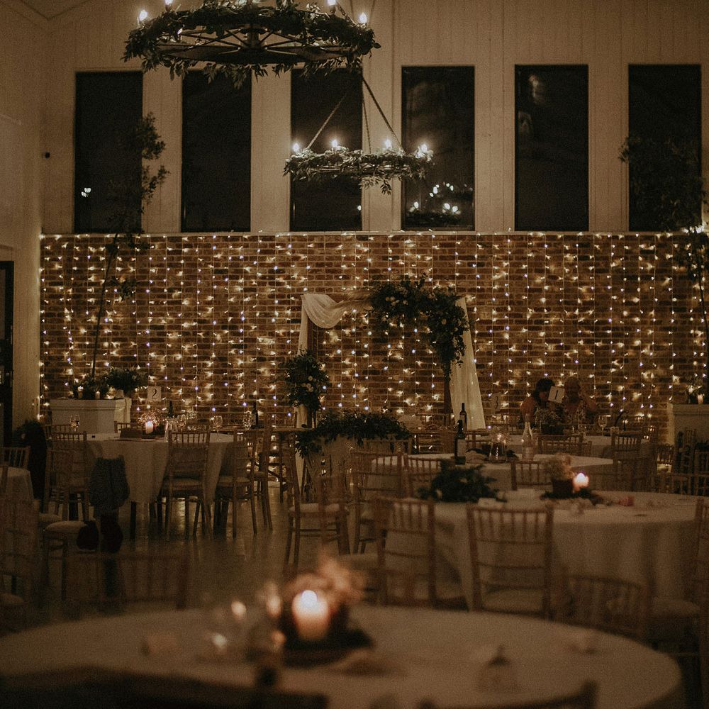 Wedding breakfast room at East Afton Farmhouse with round tables, bamboo chairs and lit by fairy lights with macrame wedding decor