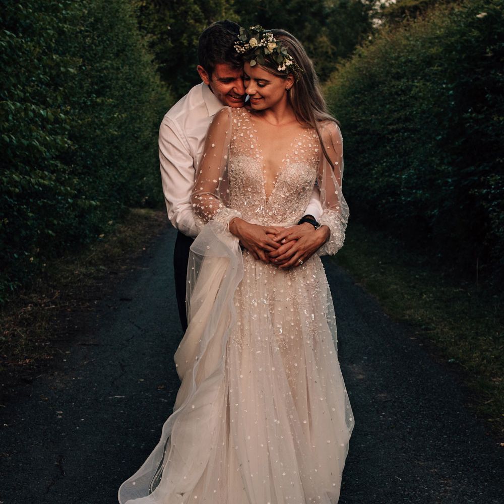 Bride in long sleeve embroidered wedding dress with boho flower crown dances with groom in white shirt and red tie during golden hour