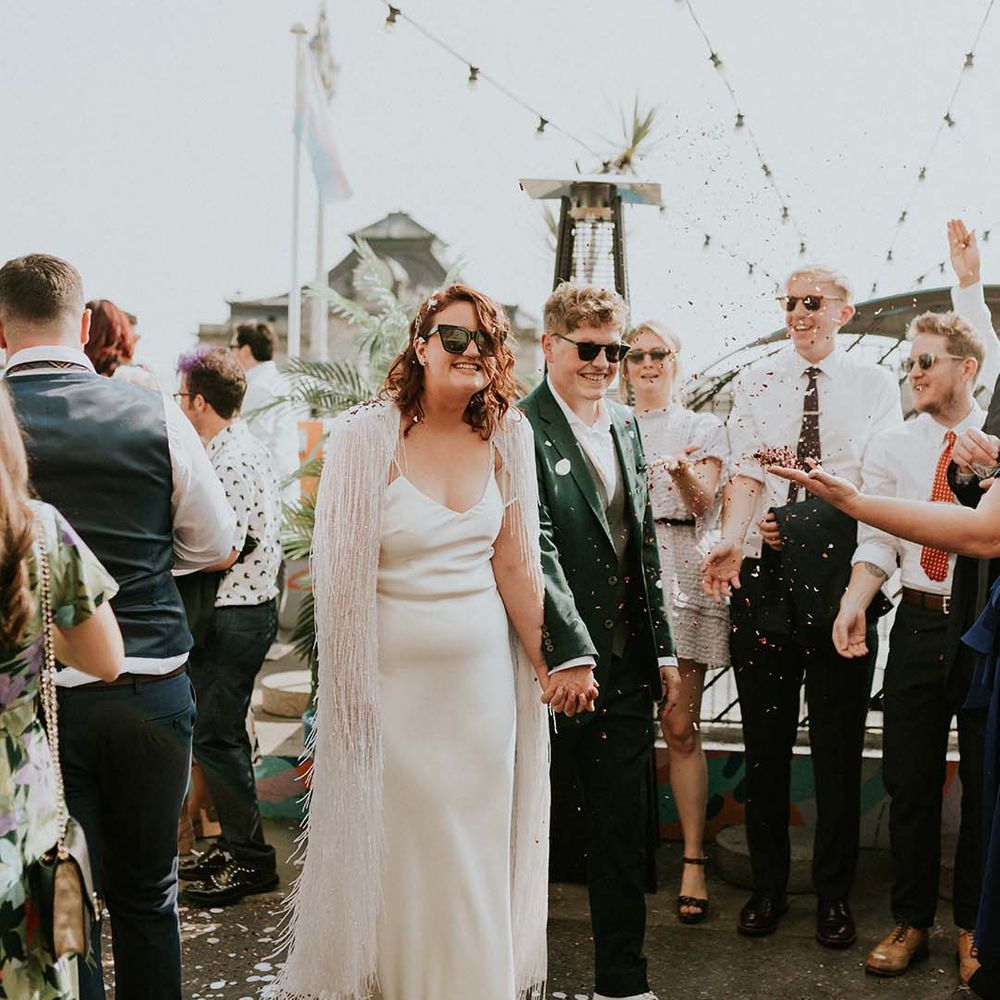 Bride & groom hold hands as they walk through confetti on their wedding day