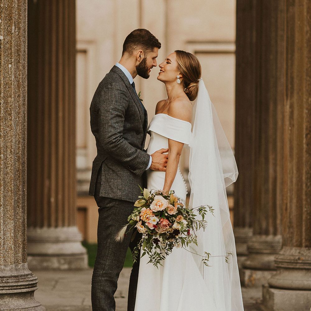 Bride & groom kiss on their wedding day as bride holds floral bouquet