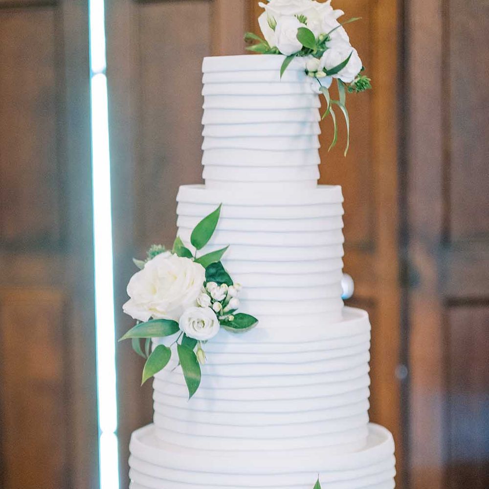 Four tier white buttercream wedding cake with white flowers and foliage decor 
