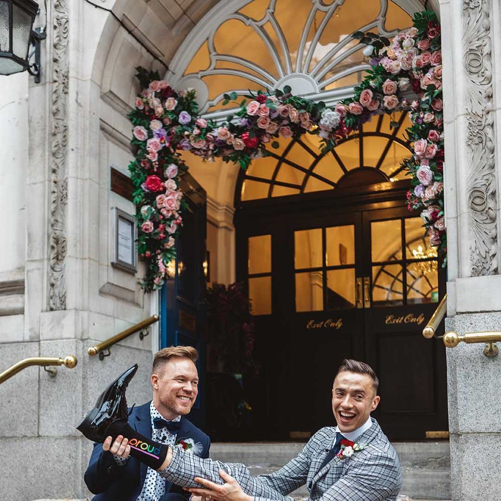 Grooms sit on steps with one another on their wedding day