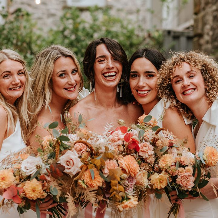 Bride smiles with her stunning bridesmaids in white one shoulder dresses